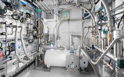 Industrieanlage mit Rohrleitungen, Tanks und Messgeräten in einer Labor-/Prozesszentrale.