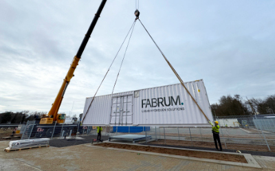 Baukran hebt Stahlcontainer mit Beschriftung “FABRUM” auf einer Baustelle.